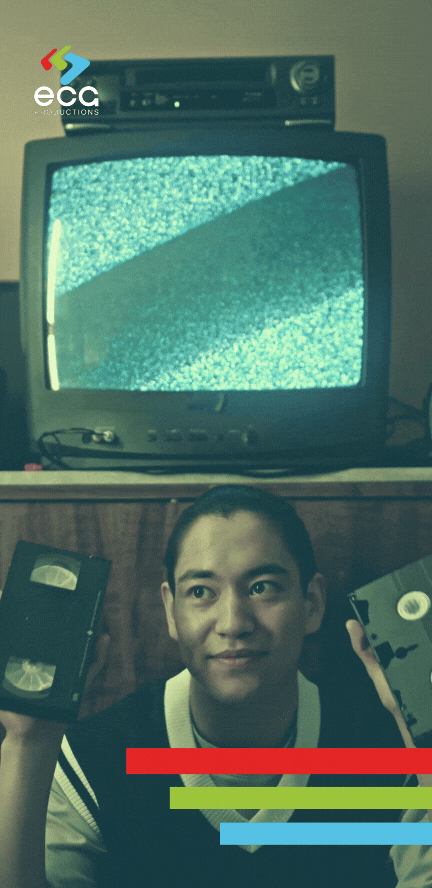 A young man sitting on the floor, holding up two VHS tapes for selection, showcasing the nostalgic connection to analog media and the importance of VHS digitization and restoration.